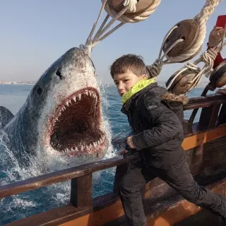 Young boy on wooden ship railing facing giant shark head