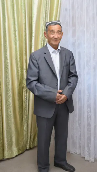 Elderly man in grey suit and traditional white cap standing